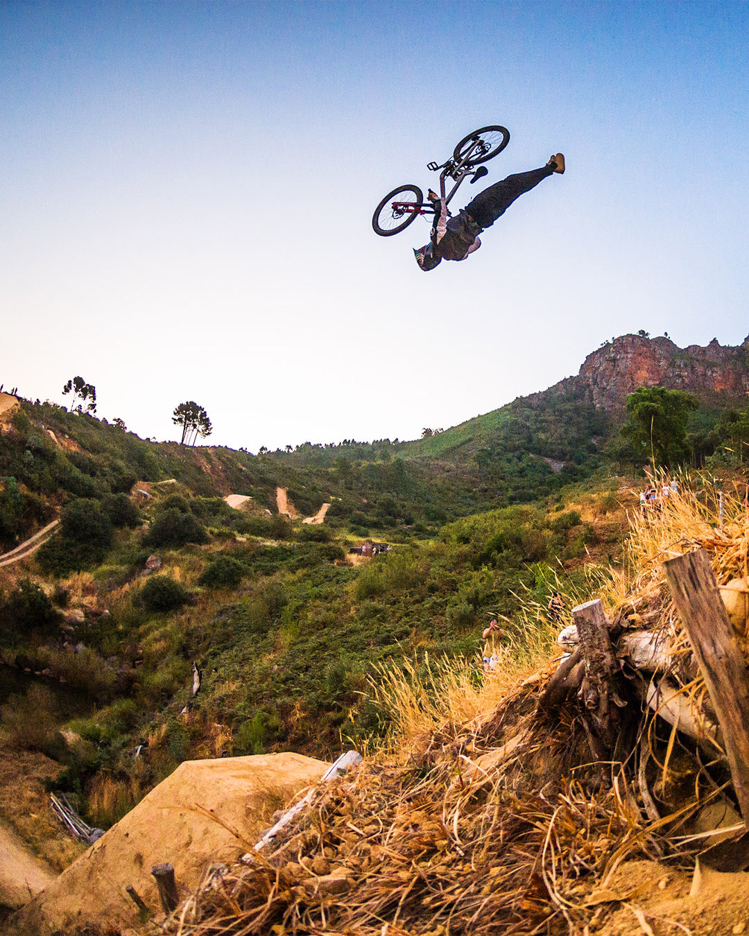 Person on a bicycle performing a jump in a mountainous landscape with clear skies.