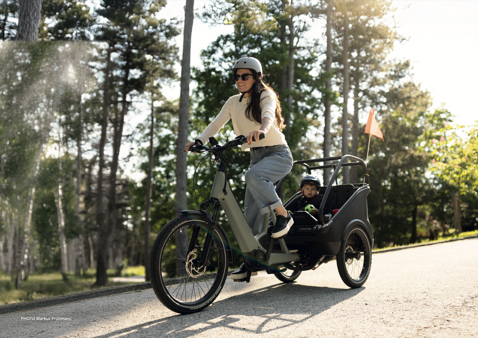 Woman riding a cargo bike with a child in a park setting