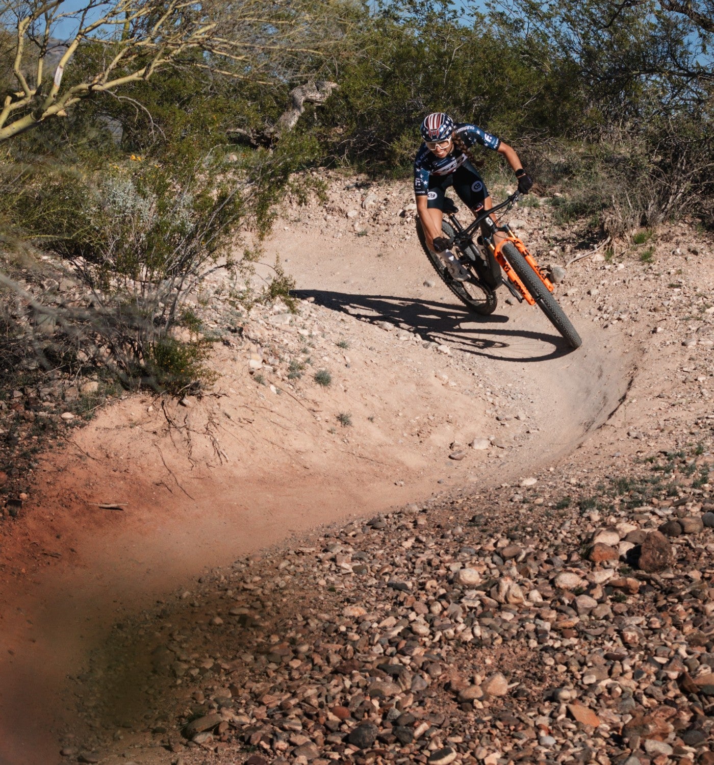Person riding an XC race mountain bike with Kenda tires on a dirt trail in a desert landscape