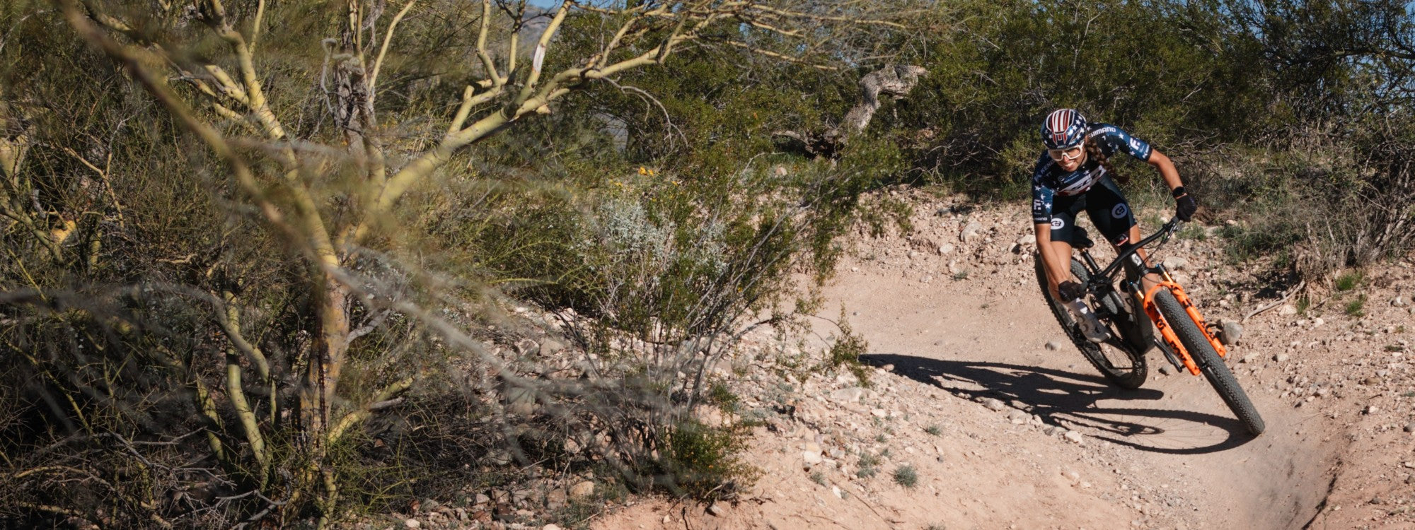 Person riding an XC race mountain bike with Kenda tires on a dirt trail in a desert landscape